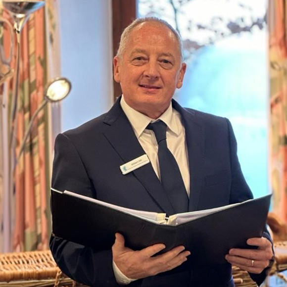 an image of William Hill in a suit standing at a podium holding a folder in preparation for a eulogy 