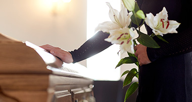 a person holding a bunch of lilies, while placing a hand on a coffin at a funeral