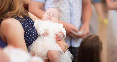 a baby in a white dress being held by a mother at a naming ceremony