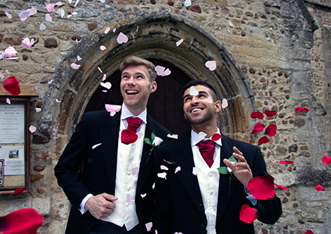 two men just married walking out of a church with flower petals showering down on them